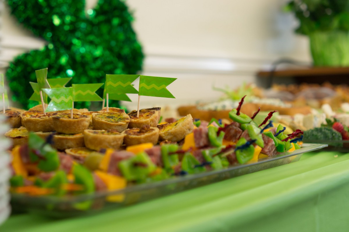 A festive table with a variety of party appetizers and green decorations.