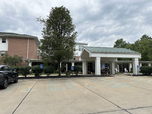 A view of a hotel entrance with a large tree and a parking area under a cloudy sky.