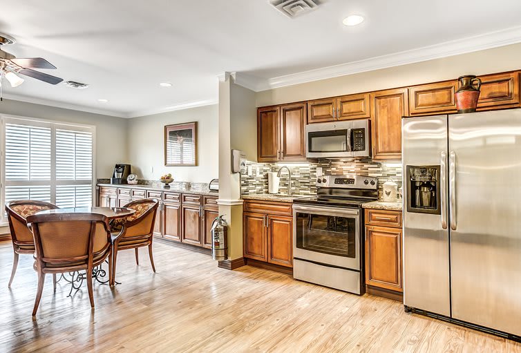 A modern kitchen with wood cabinets and stainless steel appliances, featuring an open dining area and hardwood floors.