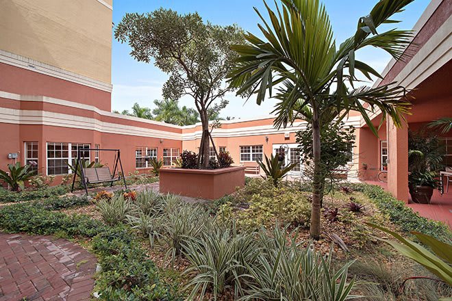 A serene courtyard garden with various plants and trees surrounded by red brick buildings.