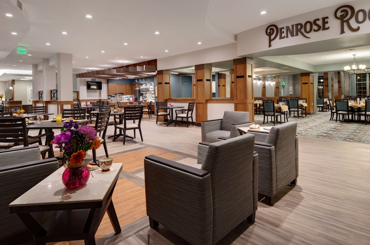 A modern restaurant interior featuring a cozy seating area with tables and chairs, accented by colorful flowers.