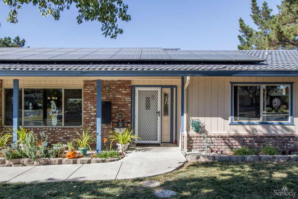 A single-story suburban house with solar panels on the roof and a front yard.
