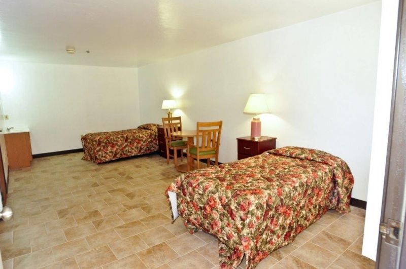 A hotel room featuring two double beds with floral bedding, a pair of lamps, chairs, and nightstands.