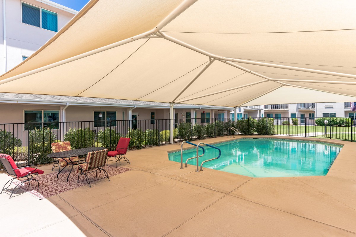 A shaded outdoor swimming pool area with patio furniture.