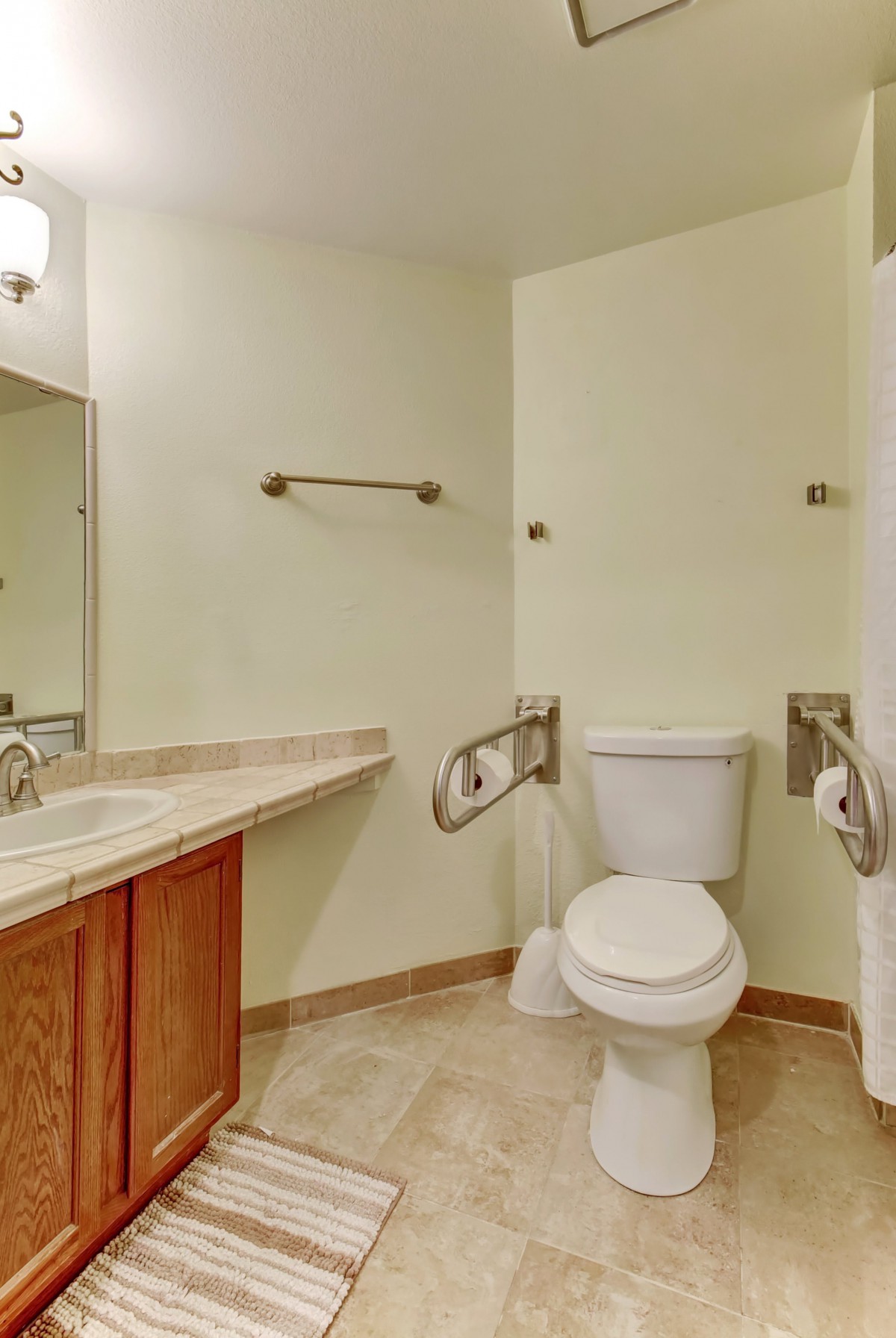 An accessible bathroom with a toilet equipped with handrails and a sink with a mirror above it.