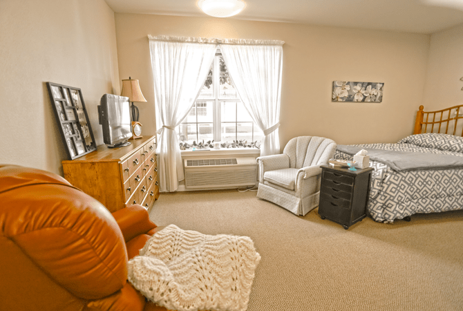 A cozy living room with armchairs, a television, and a large window with curtains.