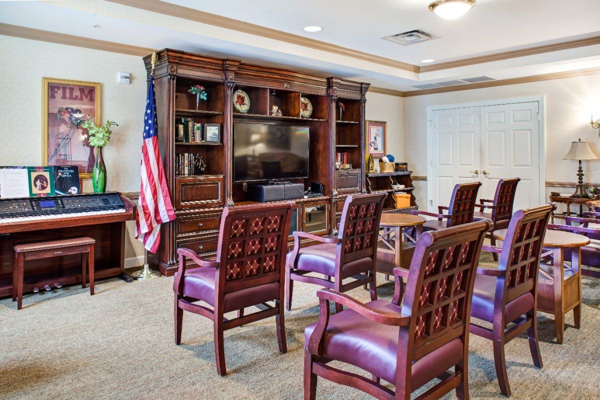 A well-furnished conference room with chairs arranged facing a large television, surrounded by bookshelves and decorative items.
