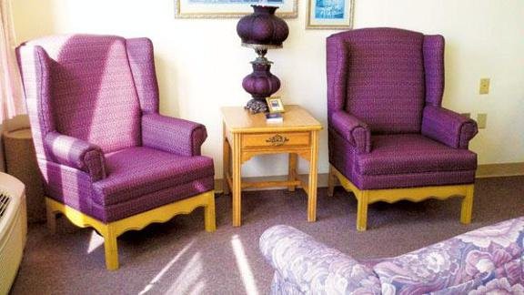 A cozy seating area featuring purple upholstered chairs and a wooden side table with a decorative lamp.