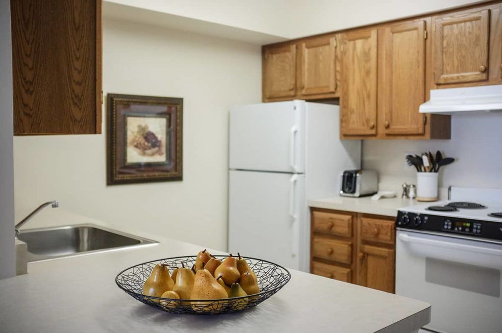A cozy kitchen with wooden cabinets, a white refrigerator, and a fruit bowl filled with pears on the countertop.