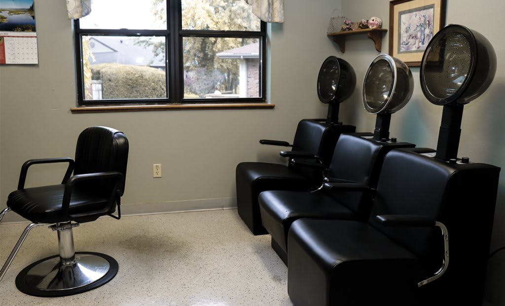 A salon interior with black chairs and hair dryers near a window.