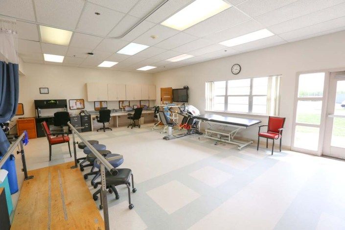 A spacious rehabilitation room equipped with exercise machines, treatment tables, and seating for patients.
