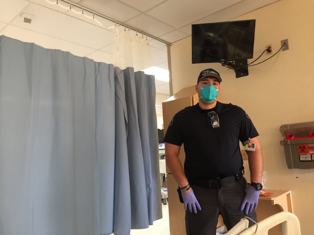 A healthcare worker wearing personal protective equipment stands in a hospital room.