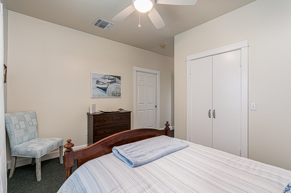 A cozy bedroom with a neatly made bed, ceiling fan, and minimalist decor.