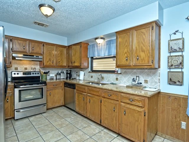 A spacious kitchen with wooden cabinets, stainless steel appliances, and a tiled floor.