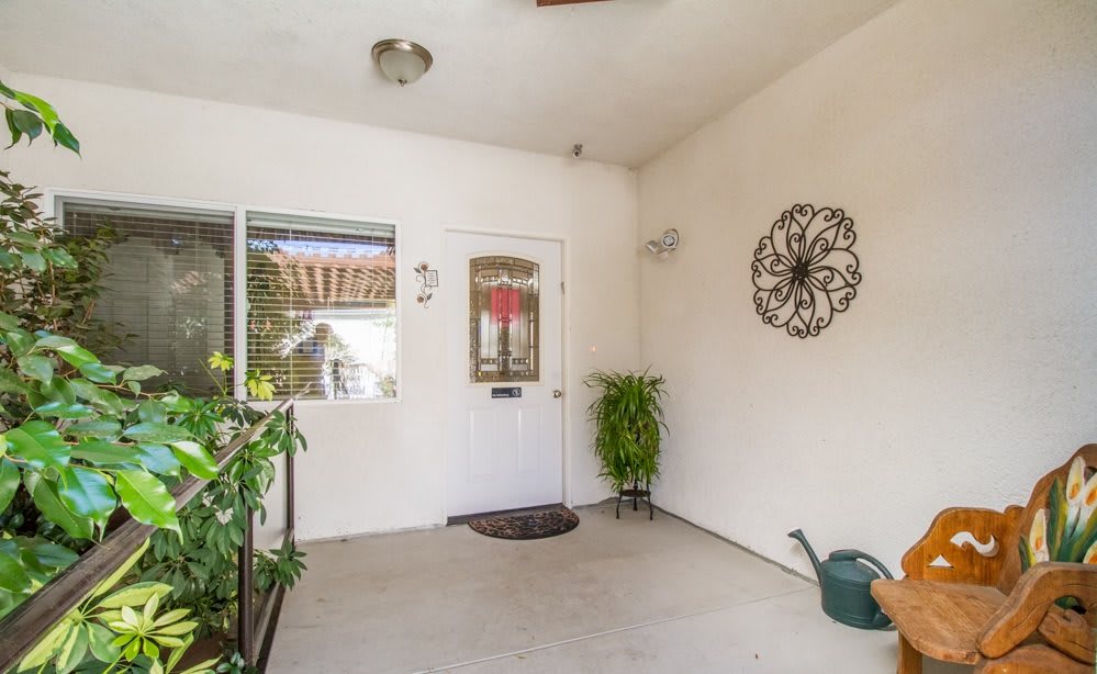 A cozy front porch with a decorated doorway, potted plants, and a wall-mounted sculpture.