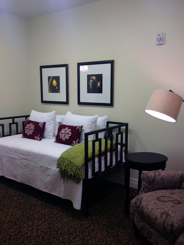 A cozy bedroom featuring a daybed, decorative pillows, framed artwork, and a standing lamp.