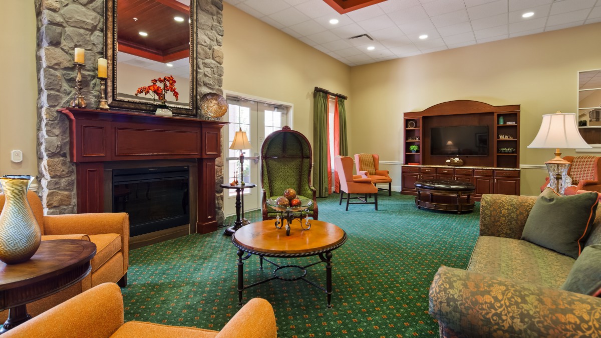 A cozy living room with a fireplace and seating area featuring orange chairs and a green carpet.