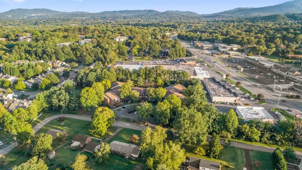 Aerial view of a suburban area surrounded by lush trees and distant mountains.
