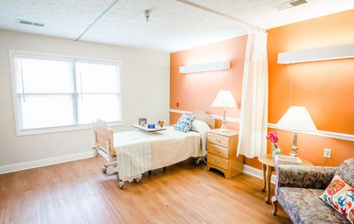 A clean and well-lit hospital room with a bed, nightstand, and window.