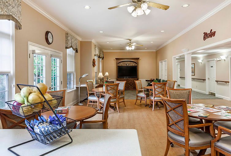 A spacious living room with multiple chairs and tables, featuring a television and ceiling fan.