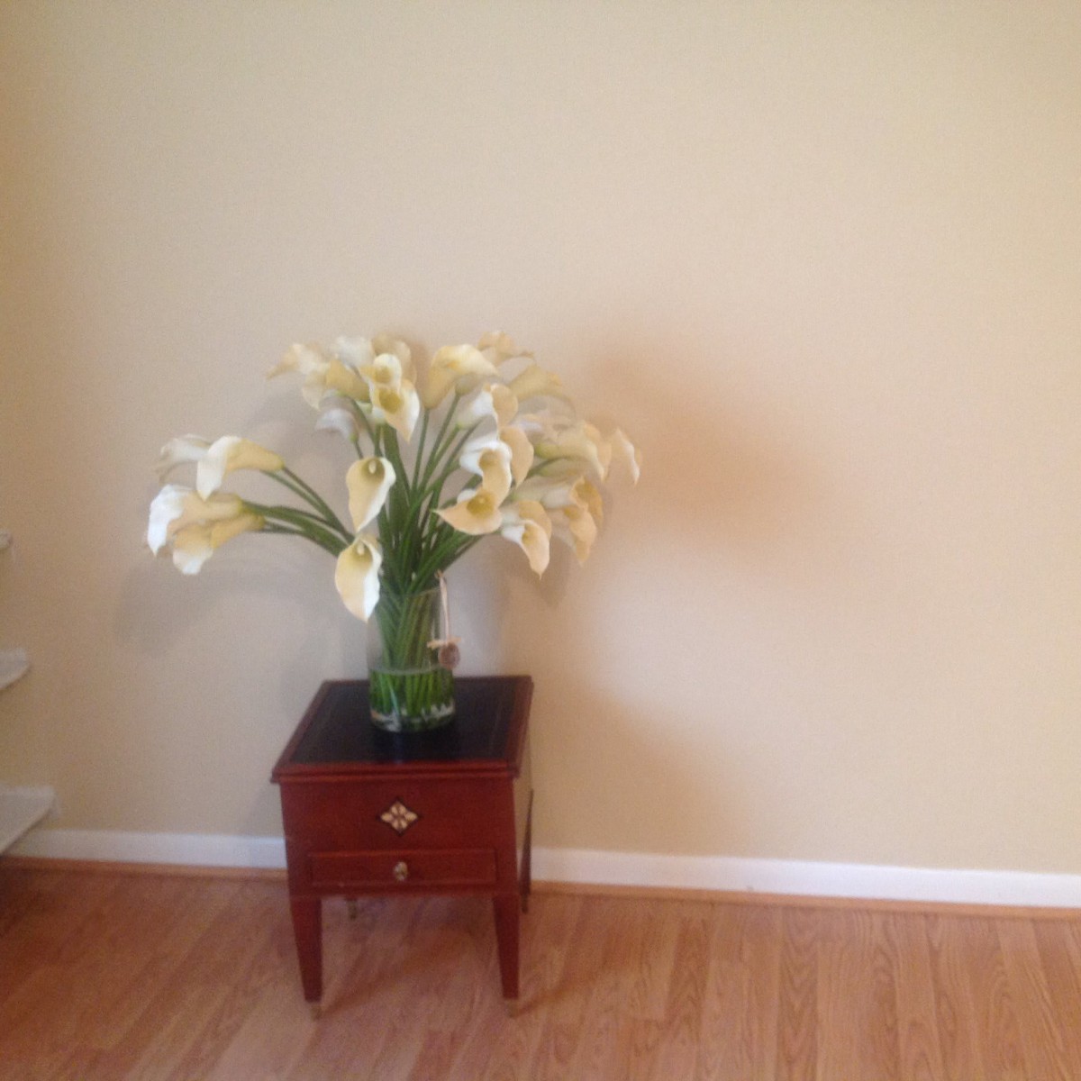 A vase of white flowers on a small wooden table against a plain wall.