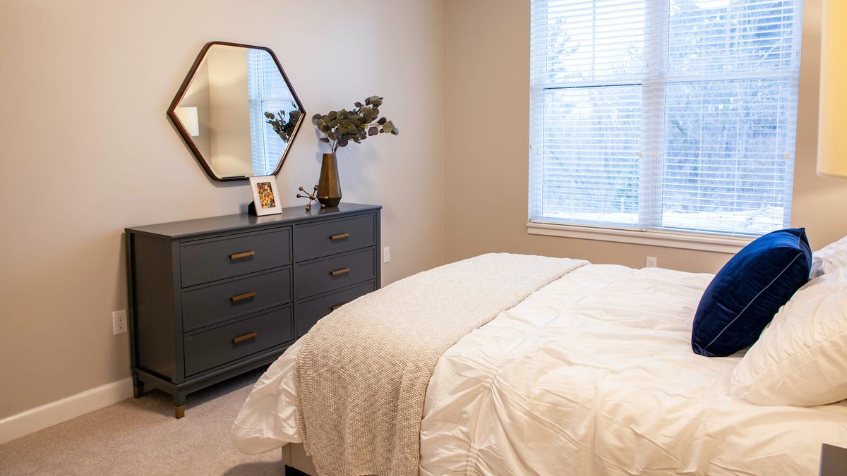 A cozy, minimalist bedroom with a stylish dresser and a hexagonal mirror on the wall.