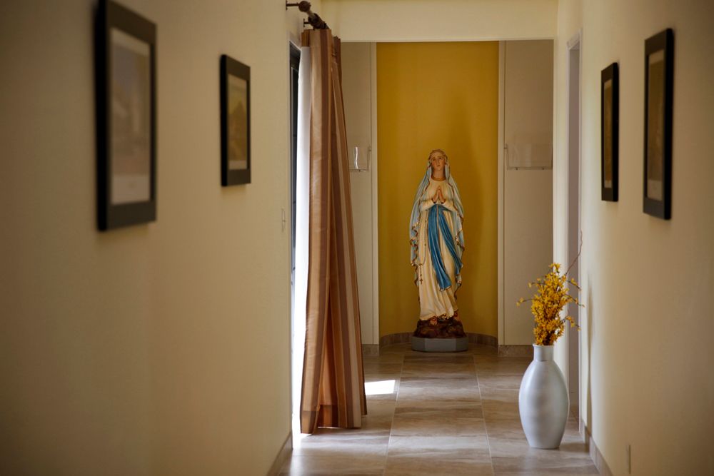 A hallway with a religious statue at the end, decorated with paintings and a vase.
