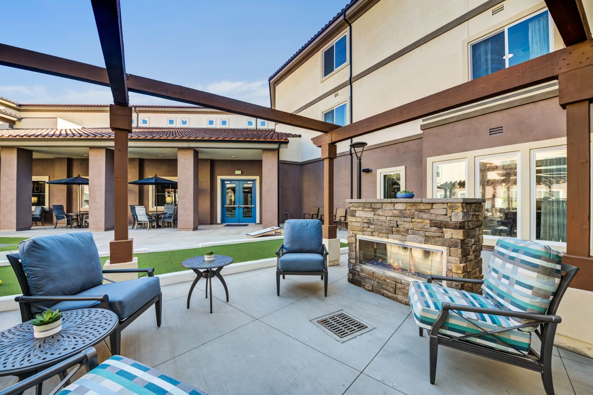 A modern outdoor patio with comfortable seating and a fireplace, set within a courtyard.