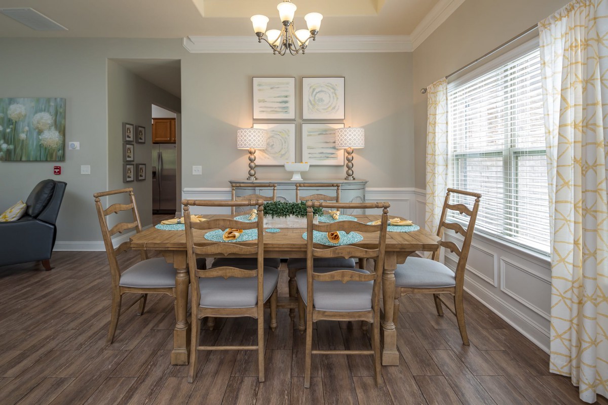 A neatly arranged dining room with a wooden table and chairs, highlighted by a chandelier and natural light from the windows.