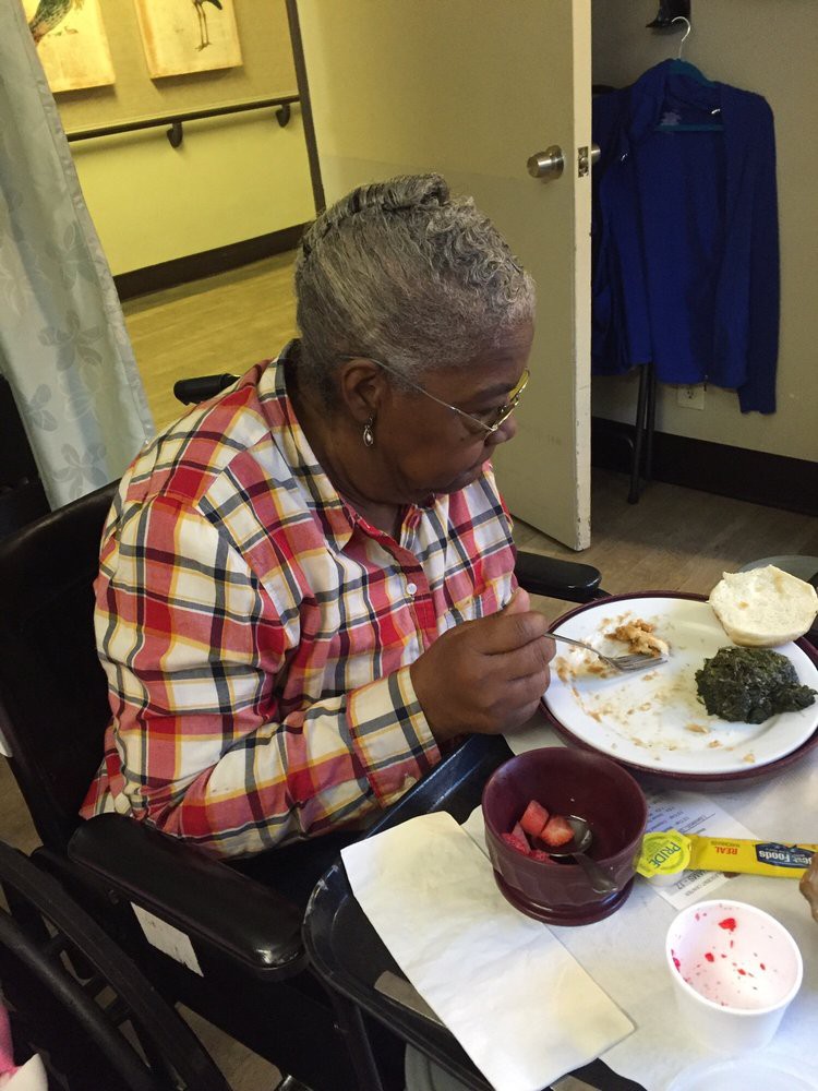 An elderly woman in a wheelchair enjoying a meal indoors.