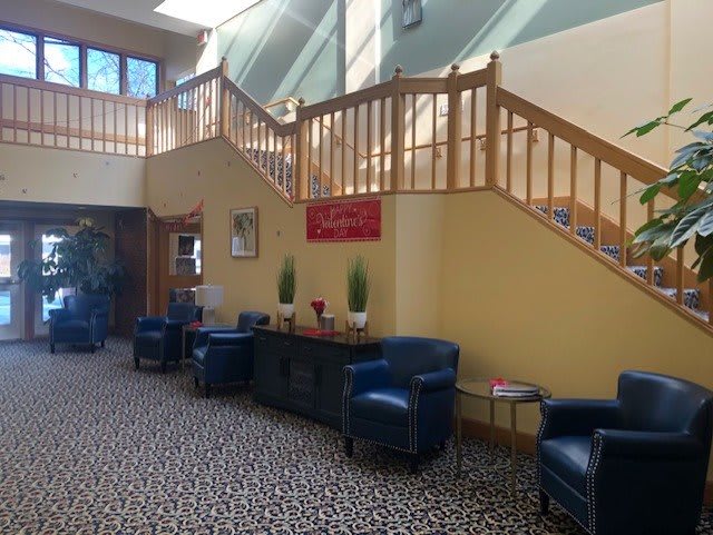 A cozy lobby area with blue chairs, a patterned carpet, and a wooden staircase leading to an upper level.