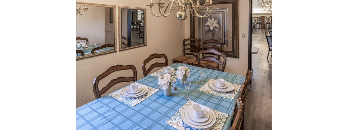 A neatly arranged dining room featuring a table with a blue checkered tablecloth, set with white dishes and a floral centerpiece under an elegant chandelier.