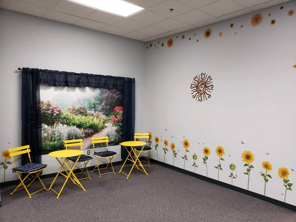 A cozy indoor seating area featuring bright yellow chairs and a garden-themed wall with sunflowers and a scenic mural.