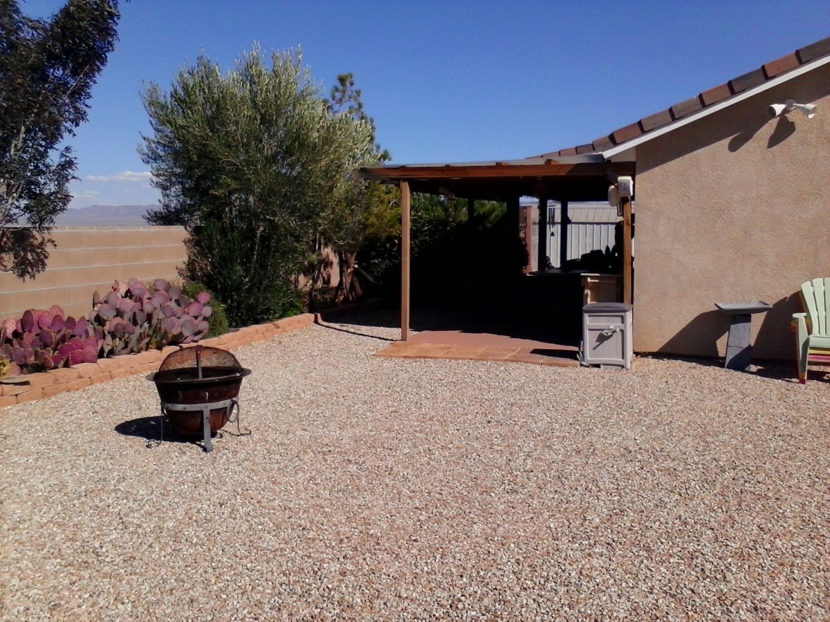A serene backyard with a gravel landscape, featuring a fire pit and covered patio area.