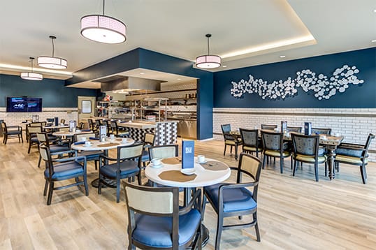 A modern restaurant interior with a stylish dining area, featuring blue walls and elegant lighting.