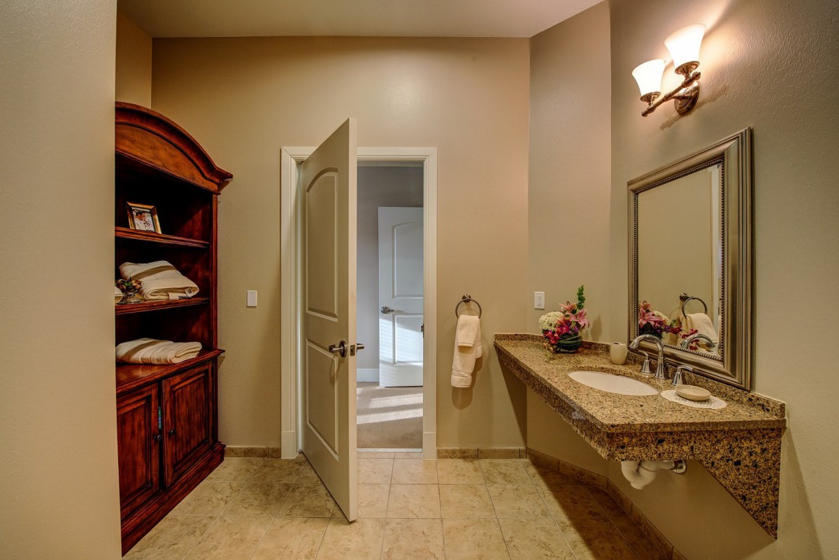 A well-lit bathroom with a double sink, mirror, and wooden cabinet, featuring towels neatly arranged on the shelf.