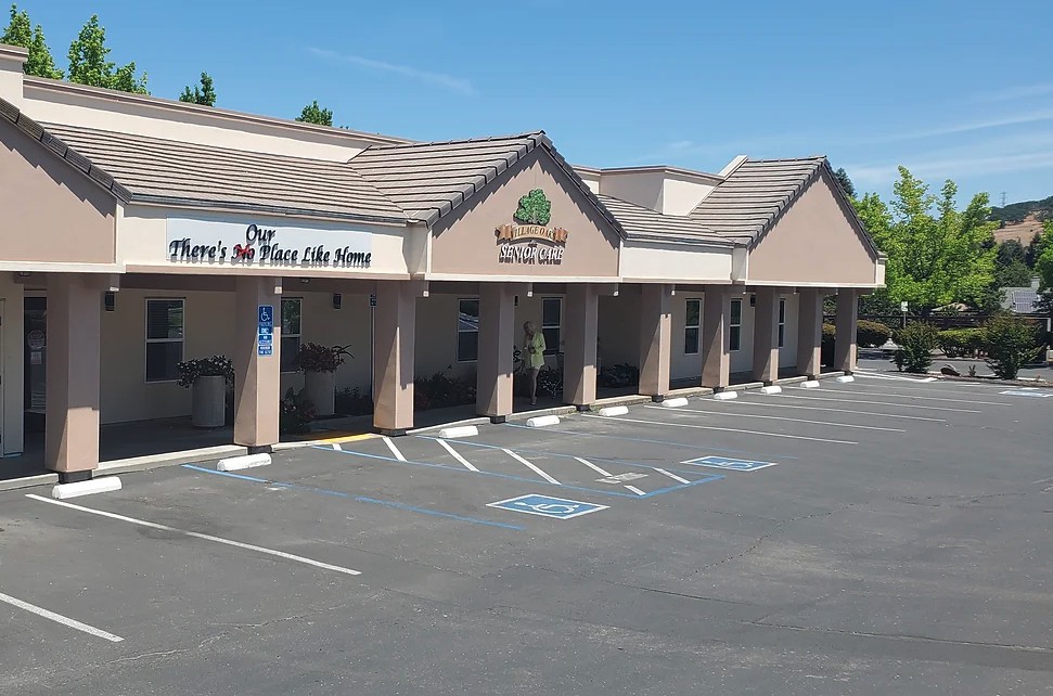 A row of storefronts in a strip mall with an adjacent parking lot on a sunny day.