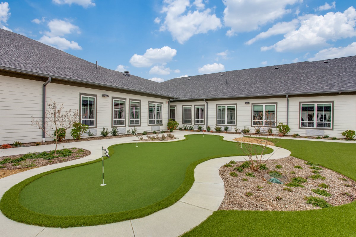 A landscaped courtyard featuring artificial turf and surrounded by a building with large windows, under a clear blue sky.