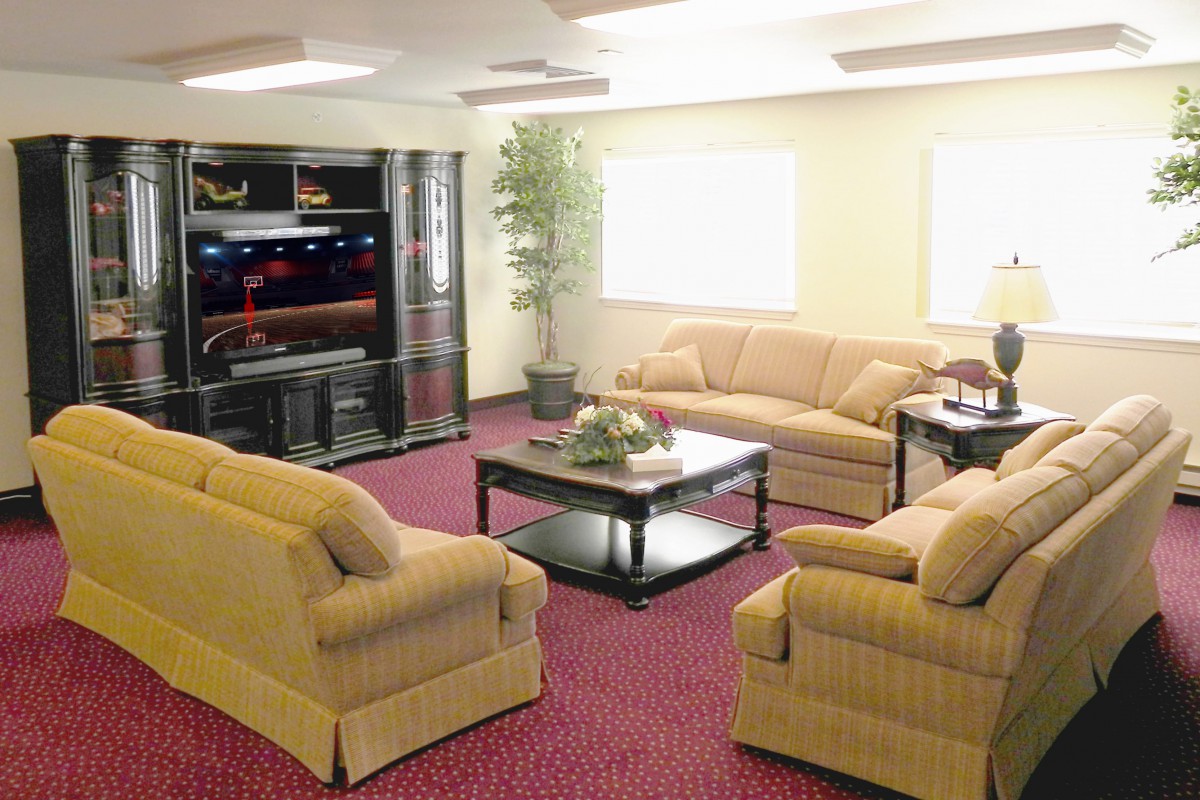 A spacious living room with beige sofas, a black coffee table, and a large television on a stand.