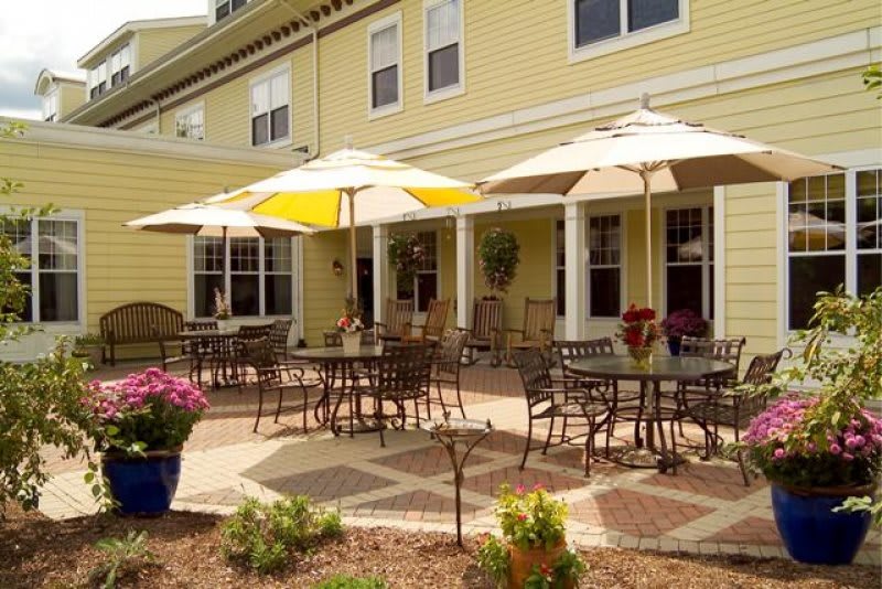 A sunny patio with tables and chairs under umbrellas in front of a yellow building.