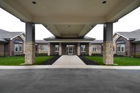 A modern building entrance featuring a covered walkway with a stone facade and surrounding landscaping.