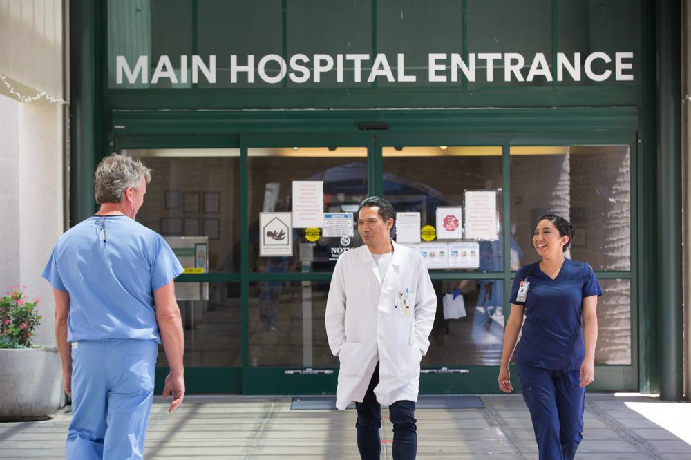 Medical staff walking in front of the main hospital entrance.