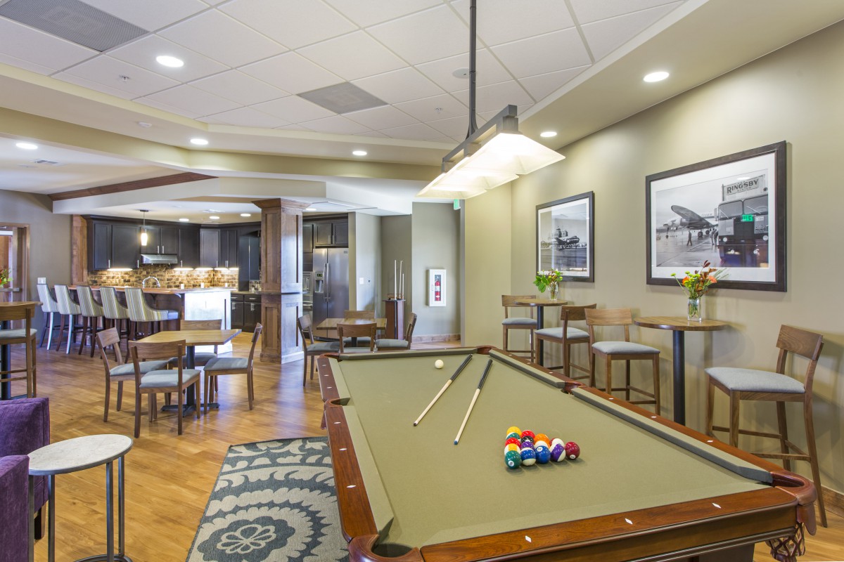 A stylish game room featuring a billiard table with cues, surrounded by comfortable seating and modern decor.
