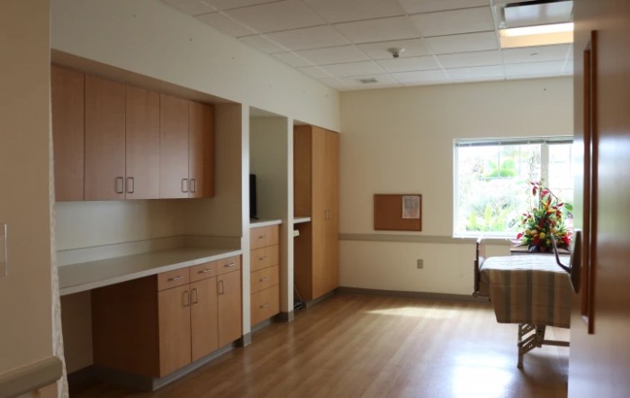 An empty hospital room with built-in cabinets and a large window letting in natural light.