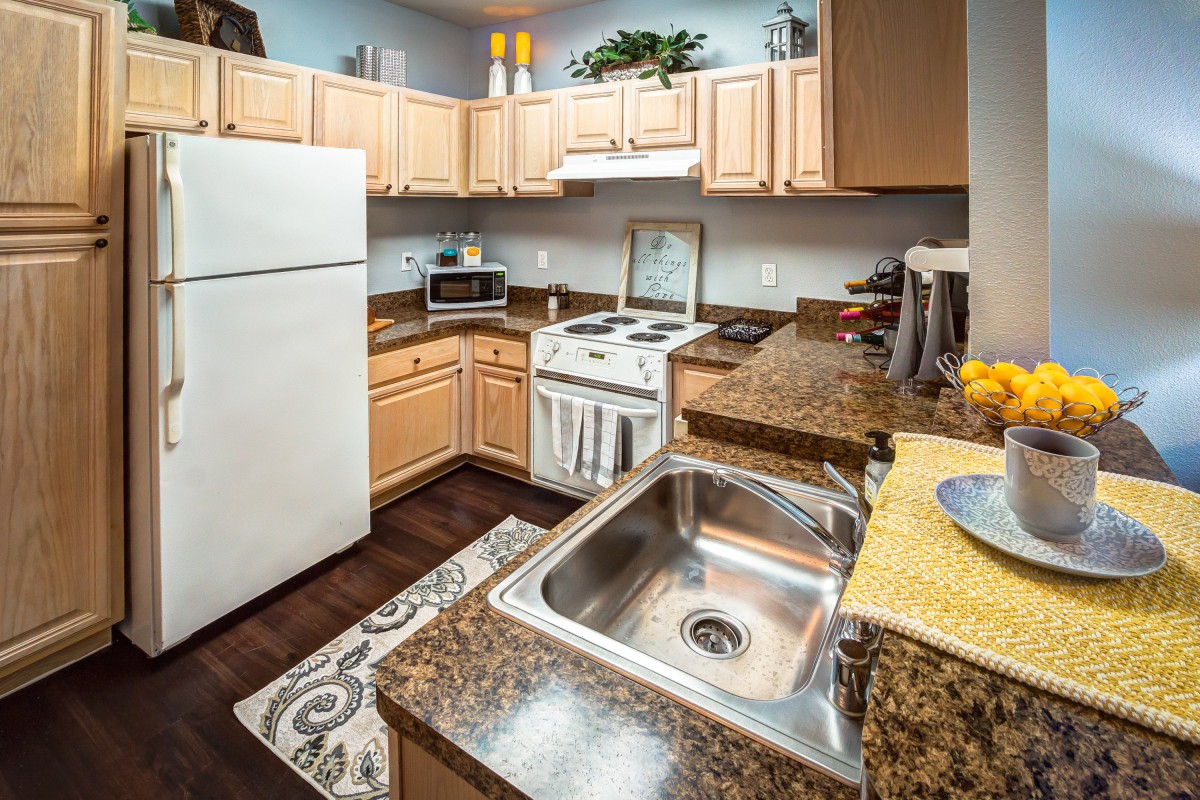 A modern kitchen interior featuring wooden cabinets, a stainless steel sink, and various appliances including an oven and refrigerator.