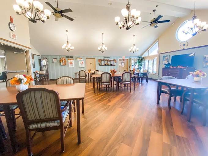 A spacious dining area with wooden flooring, featuring several tables and chairs, elegant chandeliers, and ceiling fans.