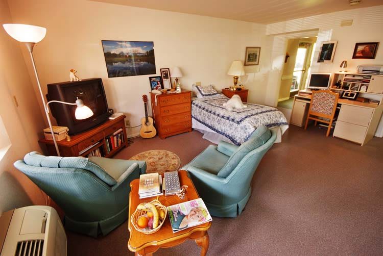 A cozy bedroom with comfortable armchairs, a bed, and a guitar by the television.