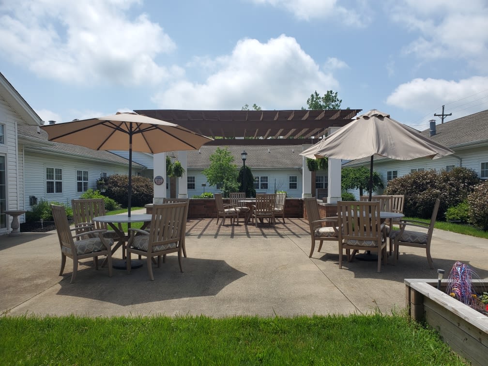A spacious outdoor patio with tables and chairs under large umbrellas, set against a sunny building backdrop.