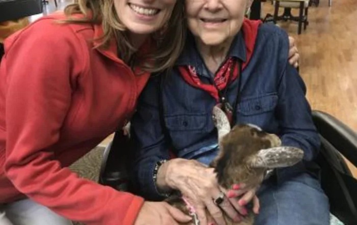 Two women smiling while holding an animal.
