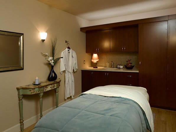 A tranquil spa massage room with a neatly made bed, soft lighting, and a robe hanging on the wall.